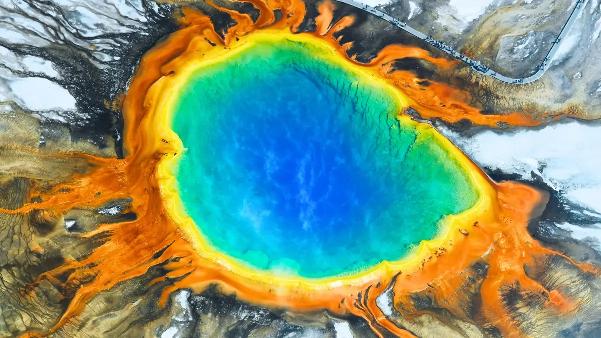 A vibrant aerial view of Thermal Pools at Yellowstone National Park, showcasing the delicate ecosystems threatened by tourists throwing coins.