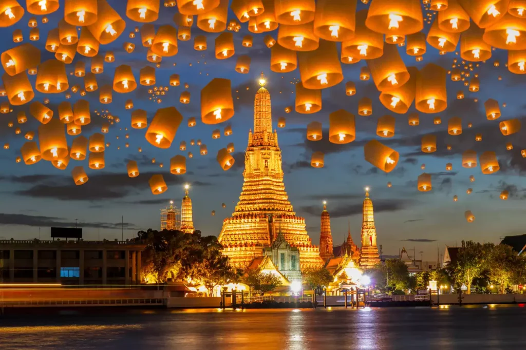 Magical sky lantern festival at Wat Arun temple in Bangkok, Thailand, illuminating the night sky.