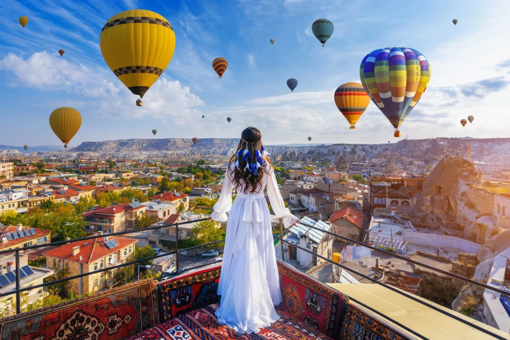 A woman in a white dress admiring hot air balloons over Istanbul, Turkey, during sunrise.