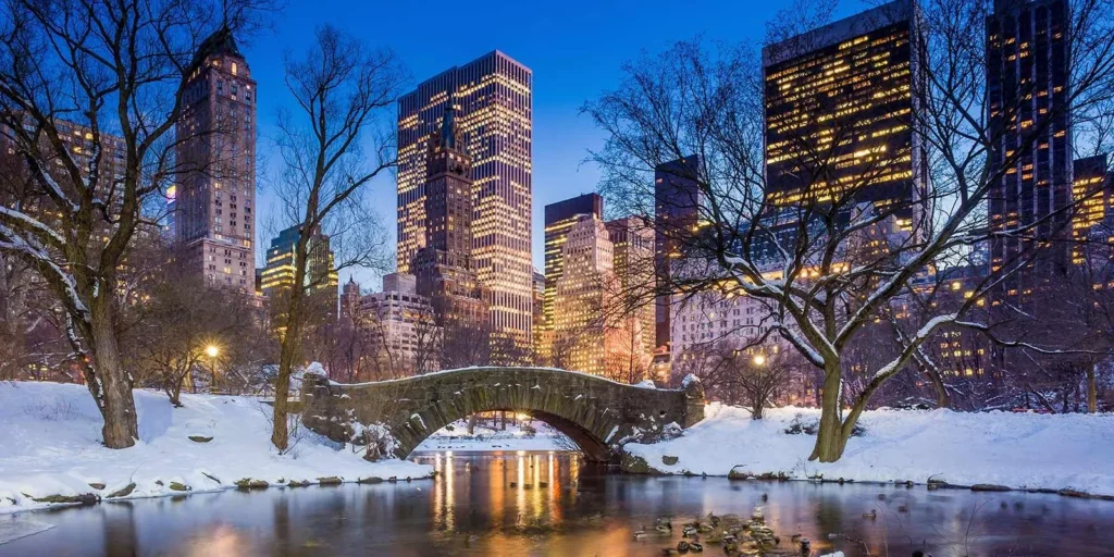 Winter evening in Central Park, New York City, with a snow-covered landscape and illuminated skyline.