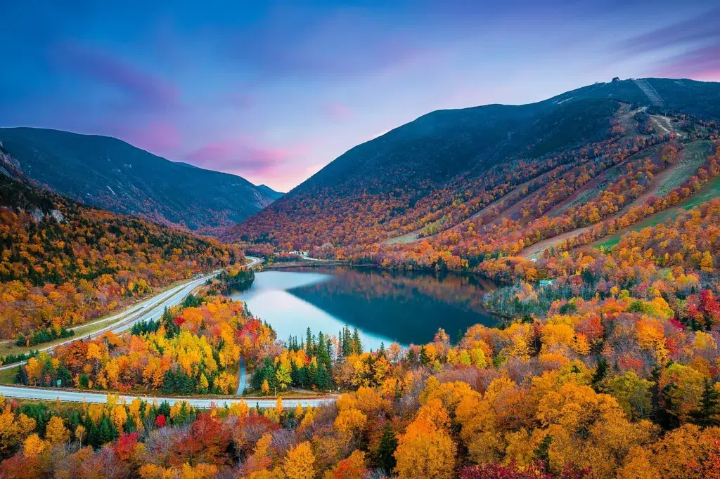 White Mountain National Forest (New Hampshire & Maine) – A breathtaking autumn landscape with vibrant foliage, a serene lake, and majestic mountains at sunset.