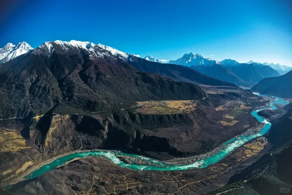 A breathtaking aerial view of Yarlung Tsangpo Grand Canyon, Tibet, China, showcasing snow-capped mountains, lush valleys, and a winding turquoise river.