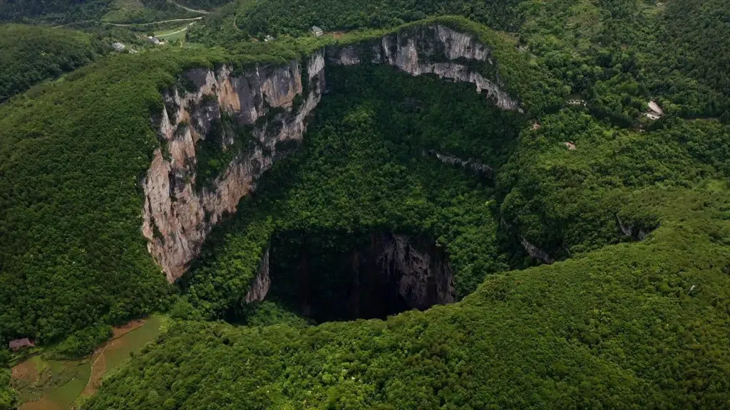 China's Giant Sinkholes – A breathtaking aerial view of a massive sinkhole surrounded by lush greenery in China’s karst landscape.